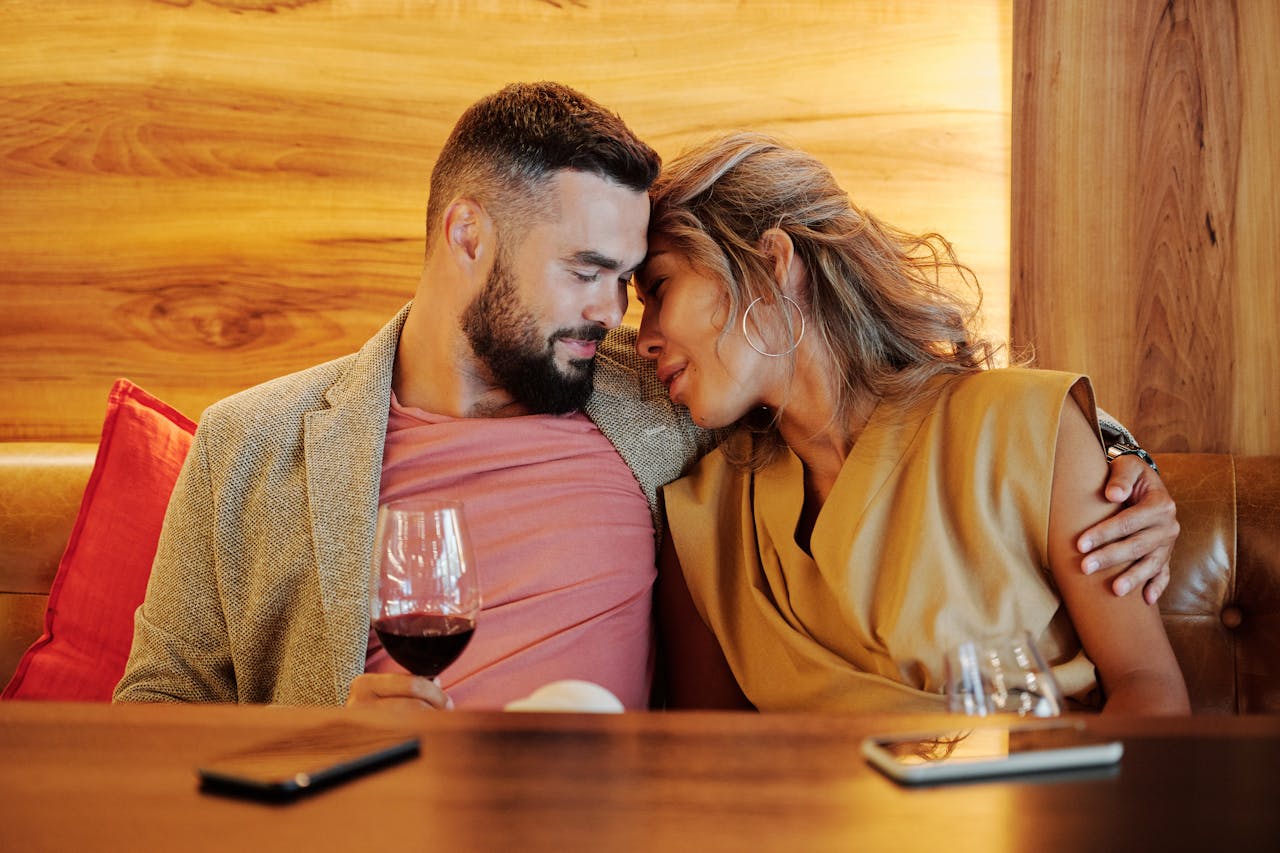 A couple shares an intimate moment with wine glasses at a cozy restaurant setting.